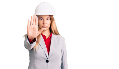 Beautiful young woman wearing architect hardhat doing stop sing with palm of the hand. warning expression with negative and serious gesture on the face.