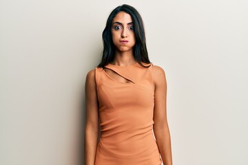 Beautiful hispanic woman wearing summer dress puffing cheeks with funny face. mouth inflated with...