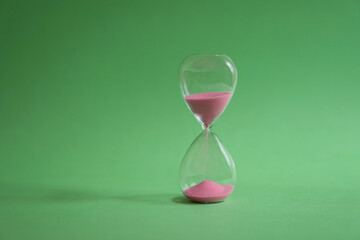 Hourglass with sand flowing on green background.