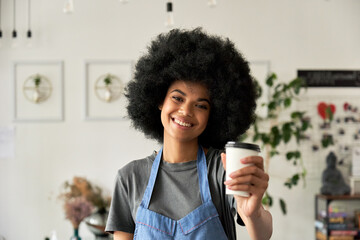Happy African American young woman with Afro hair modern cafe small business owner, female waitress, barista employee in reopened restaurant looking at camera holding takeaway coffee cup. Portrait.