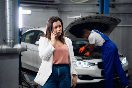 A woman is talking on the phone. Man in uniform in the background repairing a car - Powered by Adobe