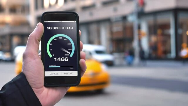 A man in New York City tests his 5G download bandwidth speed on a cellular phone. Traffic and taxi cabs pass in background. Fictional screen created in After Effects.  	