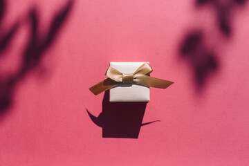 Gift box with golden bow on on pink background.Top view, flat lay, copy space. Contrasting shadows trend