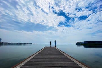 Under the background of blue sky, white clouds and lake skyline, beautiful women walk on the plank road beside the lake