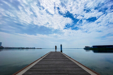 Obraz premium Under the background of blue sky, white clouds and lake skyline, beautiful women walk on the plank road beside the lake