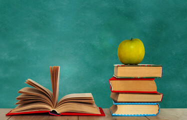 Open book textbook, pile of books and green apple on a wooden desk on the background of a green school chalkboard. Back to school distance home education.Quarantine concept of stay home.
