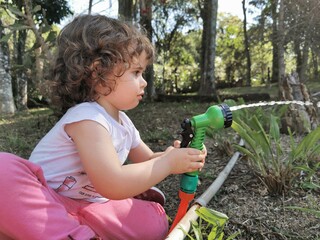 Cute Brazilian little girl having fun playing with water hose in the garden