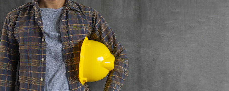 Construction worker holding safety helmet yellow on cement wall background with copy space