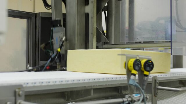 Block of cheese on assembly line picked up by machine in factory