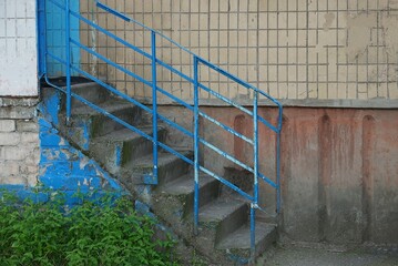 old staircase with gray concrete steps and blue iron railing against a brown wall outside