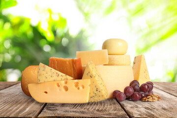 Different types of delicious cheeses on wooden table outdoors. Dairy products