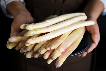 Woman holding plate with fresh white asparagus on black background, closeup