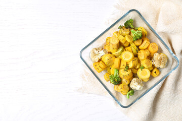 Baked yellow carrot with broccoli and cauliflowers in glass dish on white wooden table, flat lay. Space for text