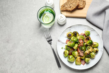 Delicious fried Brussels sprouts with bacon served on grey table, flat lay. Space for text