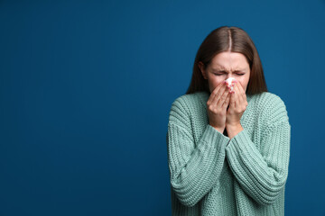 Young woman sneezing on blue background, space for text. Cold symptoms