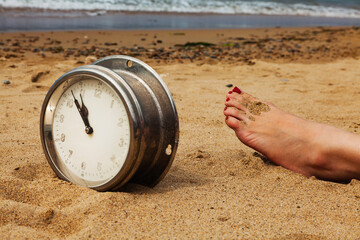 Old round ship clock on the sand and the foot of a sunbathing girl on the beach, summer by the sea,...