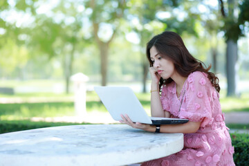 A beautiful woman sitting in the park working Clearing out the tasks that were not ordered as needed.