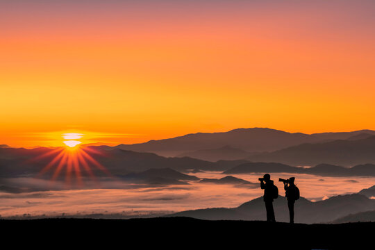 Silhouette image of a traveler man and woman taking photos with sunrise in the morning on mountains natural background.