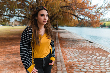 A young woman standing at autumnal park and looking at lake. Medium shot