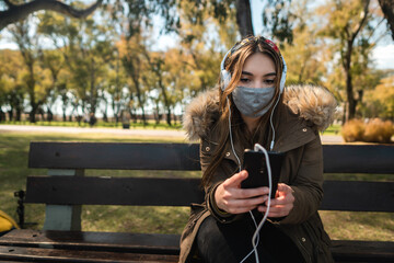 A caucasian woman wearing face mask sitting on a bench and using her smartphone. Copy space