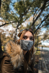 A woman wearing face mask sitting at park and looking at camera during covid 19 pandemic. Vertical