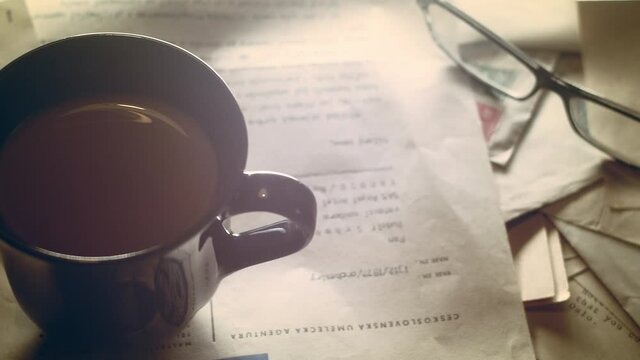 Old Documents And Letters Scattered On The Wooden Table With Eye Glasses, Cigarette, And A Cup Of Hot Coffee. - high angle - panning shot