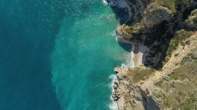 Aerial top down view of a beautiful beach with turquoise waters between the cliffs in the mediterranean coast of Spain.