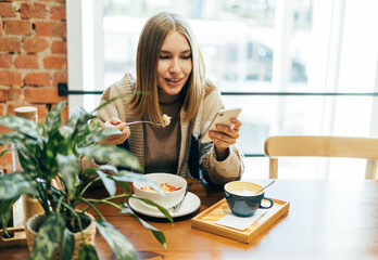 Young blonde woman in casual clothing look at smatphone during lunch at the cafe
