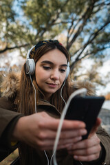 Close up of a caucasian woman using headphones and texting with her smartphone at park