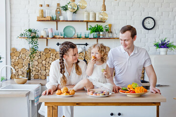 Family portrait of a happy mother, daughter and father posing in the kitchen during Breakfast, eating delicious macaroons, cakes, cookies. Married good relations, love each other