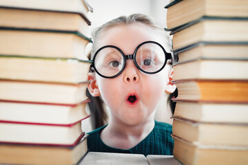 Shocked little blonde kid girl 4-6 years old in library among many books. Back to school concept.