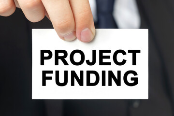 Businessman shows a card with the text - PROJECT FUNDING