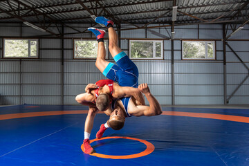 Two young sportsmens wrestlers in red and blue uniform wrestling against wrestling carpet, view side