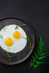 Breakfast with two fried eggs and herbs on black background