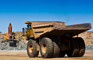 Obraz premium Mining scene. Large truck drives towards digger to fill with ore from open cast mine. All logos removed.