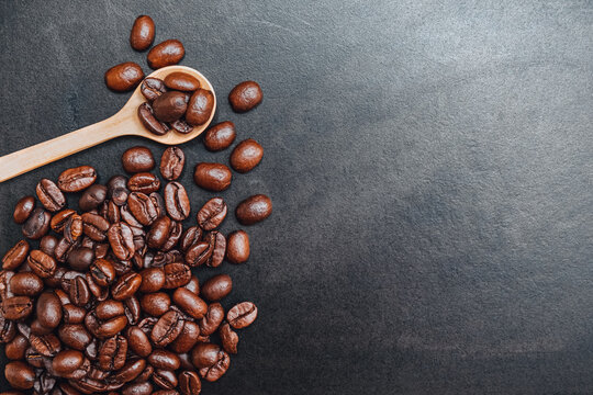 Wooden spoon with dark roasted coffee beans on blackboard background. Photos from the top view and copy space. Seed nature from the above view. Group agriculture grain arabica. Top-down