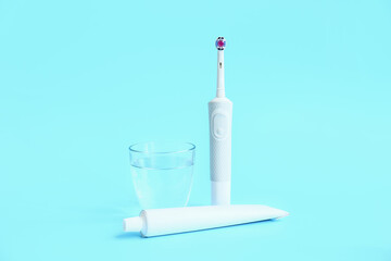 Electric tooth brush, glass of water and paste on color background