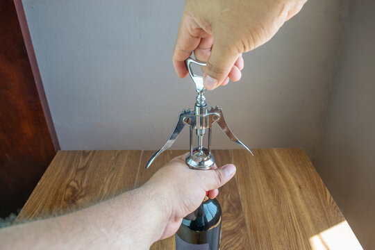 Man Uncorking Bottle Of Red Wine With Corkscrew