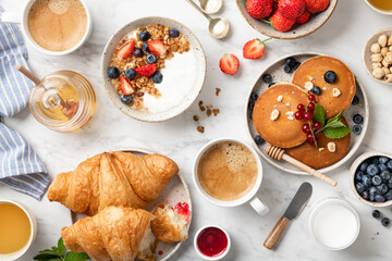 breakfast top view, pancakes, croissants, granola with yogurt, berries, nuts and coffee on a white...