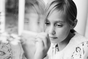 Young girl looking through the window. Quarentine concept