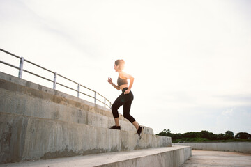 Fitness Asian woman with fit body running up the stairs in sunrise outdoor.