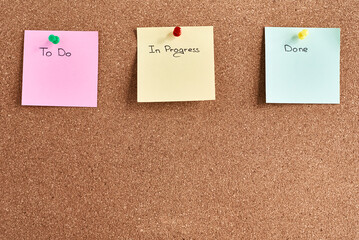 Three sticky notes pinned on a cork board with inscriptions to do, in progress and done. Planning...
