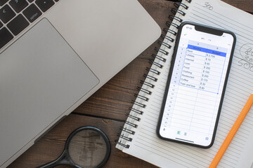 Smartphone with monthly budget list on wooden table. Home budget planning concept top view. Home...