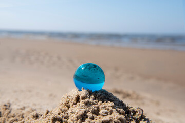 Blue glass ball on sand near the sea. Abstract conceptual photo.
