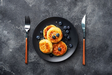 Fritters of cottage cheese with blueberries. Cheese curd cheesecakes, pancakes on a dark concrete background. Copy space.
