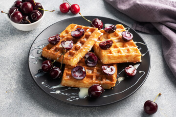 Belgian fluted waffles with fresh cherries and cream on a plate. Soft homemade waffles, sweet dessert with cherries.