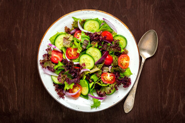 Healthy vegetable salad of cherry tomatoes, cucumber slices, green and purple lettuce leaves, onions and olive oil in plate on wooden table Top view Flat lay Diet, mediterranean menu Vegan food