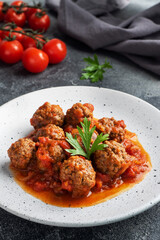 Beef meatballs stewed in tomato sauce on a plate. Dark concrete background.