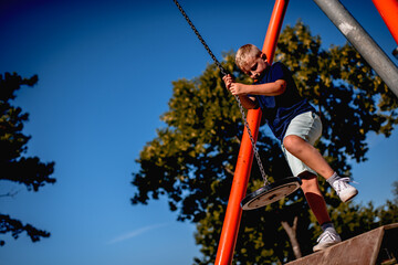 Young boy playing on a zip line at obstacle course in public park during summer day