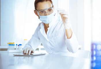 Female laboratory assistant analyzing test tube with blue liquid. Medicine, health care and researching concept